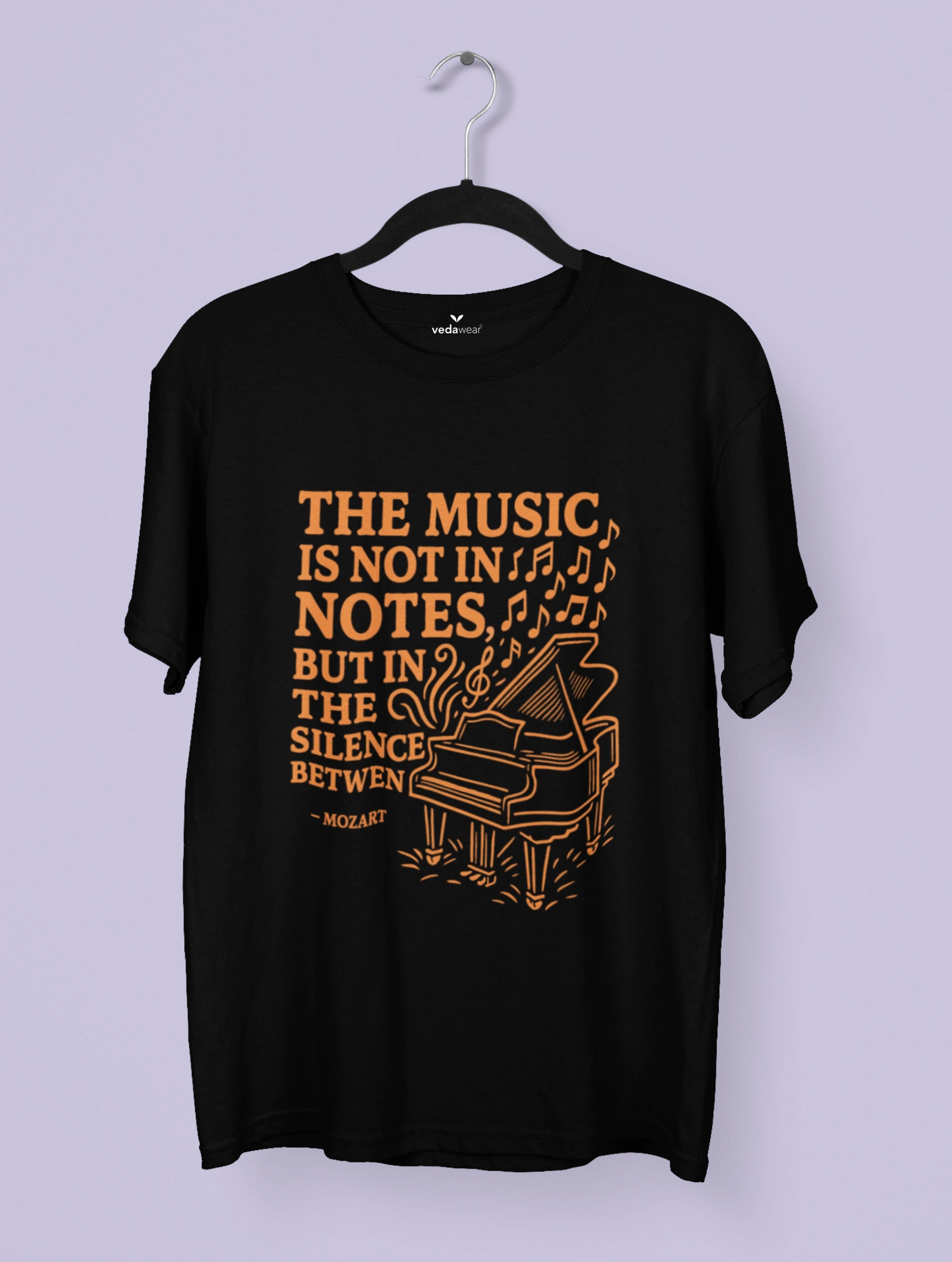 Black t-shirt with orange text and piano graphic on a hanger against a light purple background