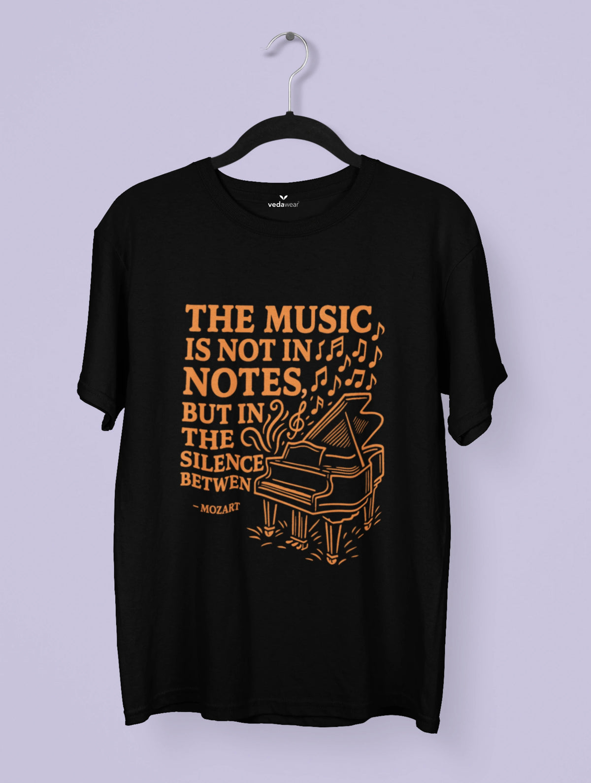 Black t-shirt with orange text and piano graphic on a hanger against a light purple background